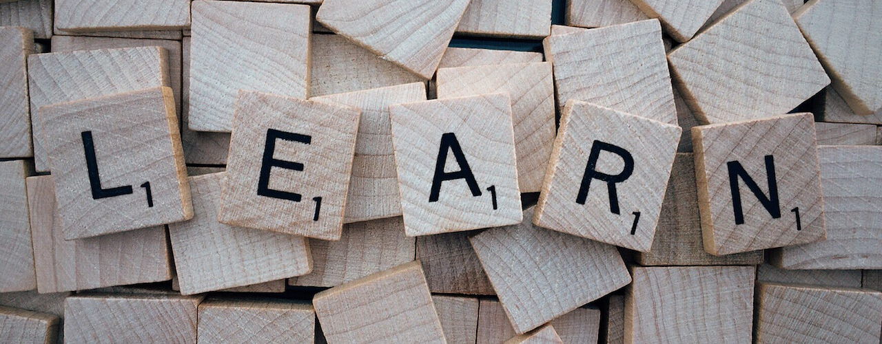 Scrabble-Steine bilden das Wort 'LEARN' auf einem Hintergrund von weiteren Scrabble-Steinen