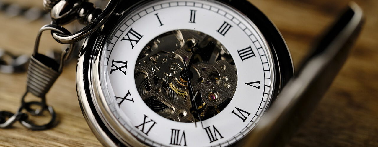 Eine geöffnete Taschenuhr mit römischen Ziffern und sichtbarem Uhrwerk liegt auf einer Holzoberfläche